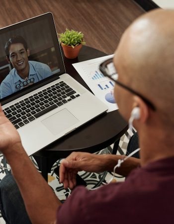 Online business meeting Young businessman in earphones having online meeting with Vietnamese colleague and discussing company development